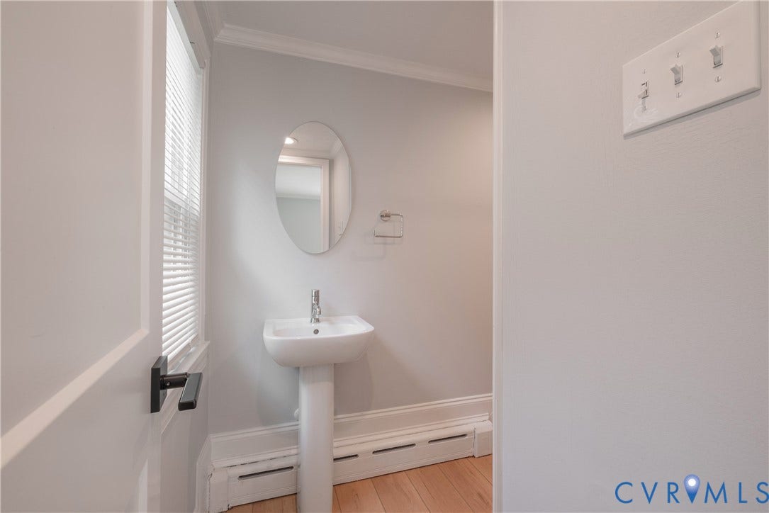 5709 Monument Avenue, Richmond, VA 23226 Lower level full bath Pedestal sink with chrome faucet, oval mirror, and window with horizontal blinds