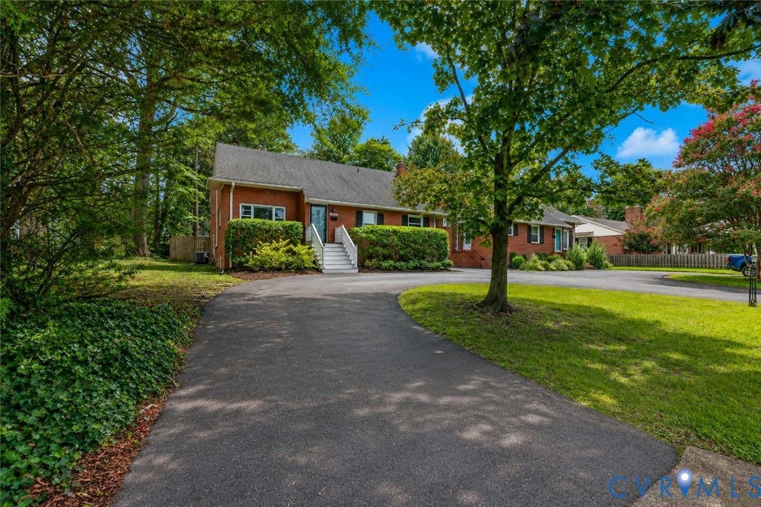5709 Monument Avenue, Richmond, VA 23226 Brick exterior residence featuring a dark shingle roof, established landscaping, white exterior stairs, and an asphalt driveway
