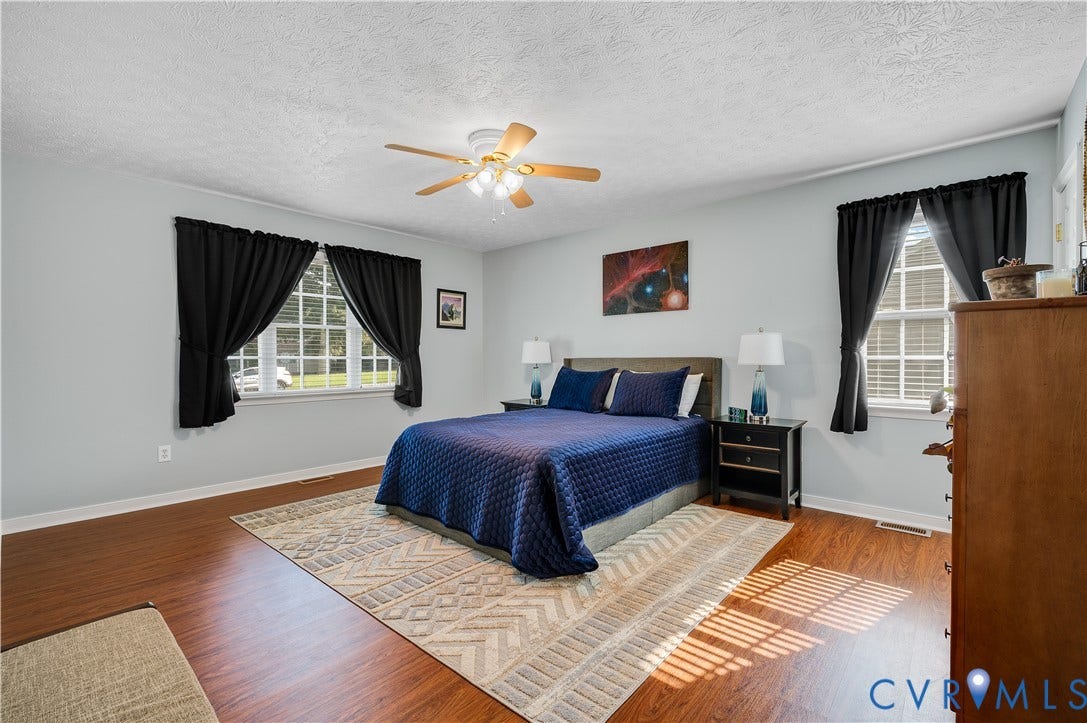 3117 Pinefields Drive, Henrico, VA 23231 Spacious primary bedroom featuring hardwood flooring, a ceiling fan with integrated lighting, and abundant natural light from multiple windows.