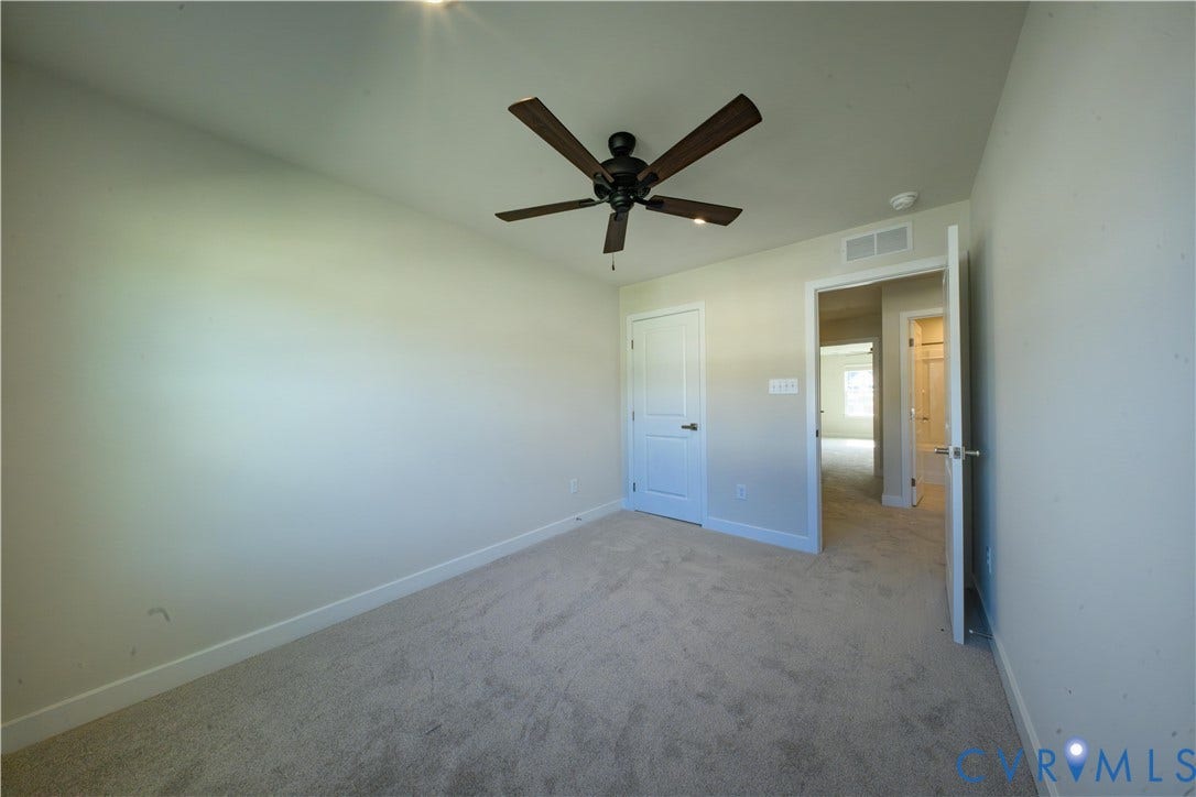 Ceiling fan with wood-finish blades, light neutral wall paint, and light-colored carpeting