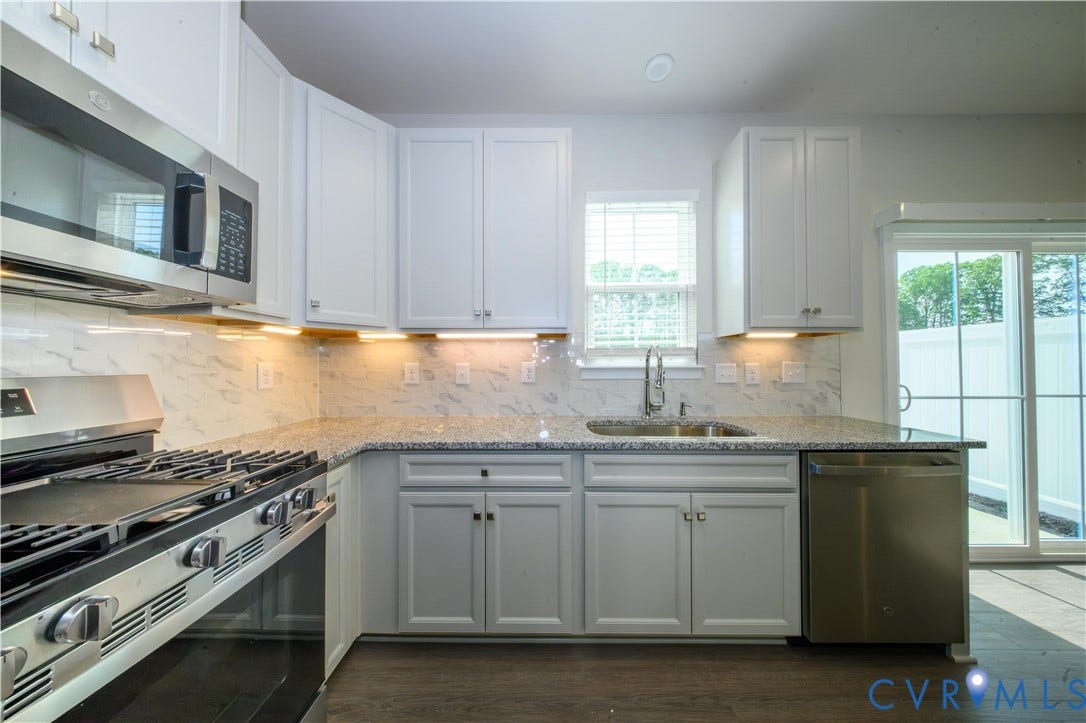 Kitchen featuring white shaker cabinetry, granite countertops, a tile backsplash, stainless steel appliances, and a sliding glass door
