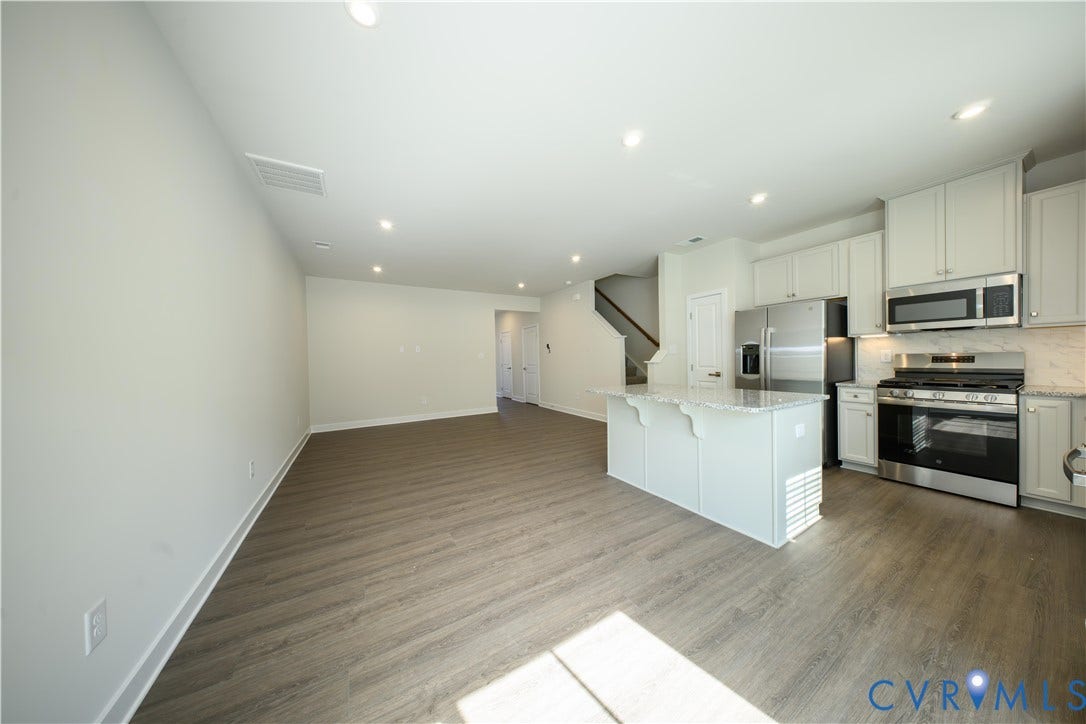 Open-concept living space featuring wood-finish flooring, recessed lighting, a kitchen island with stone countertop, stainless steel appliances, and a tiled kitchen backsplash
