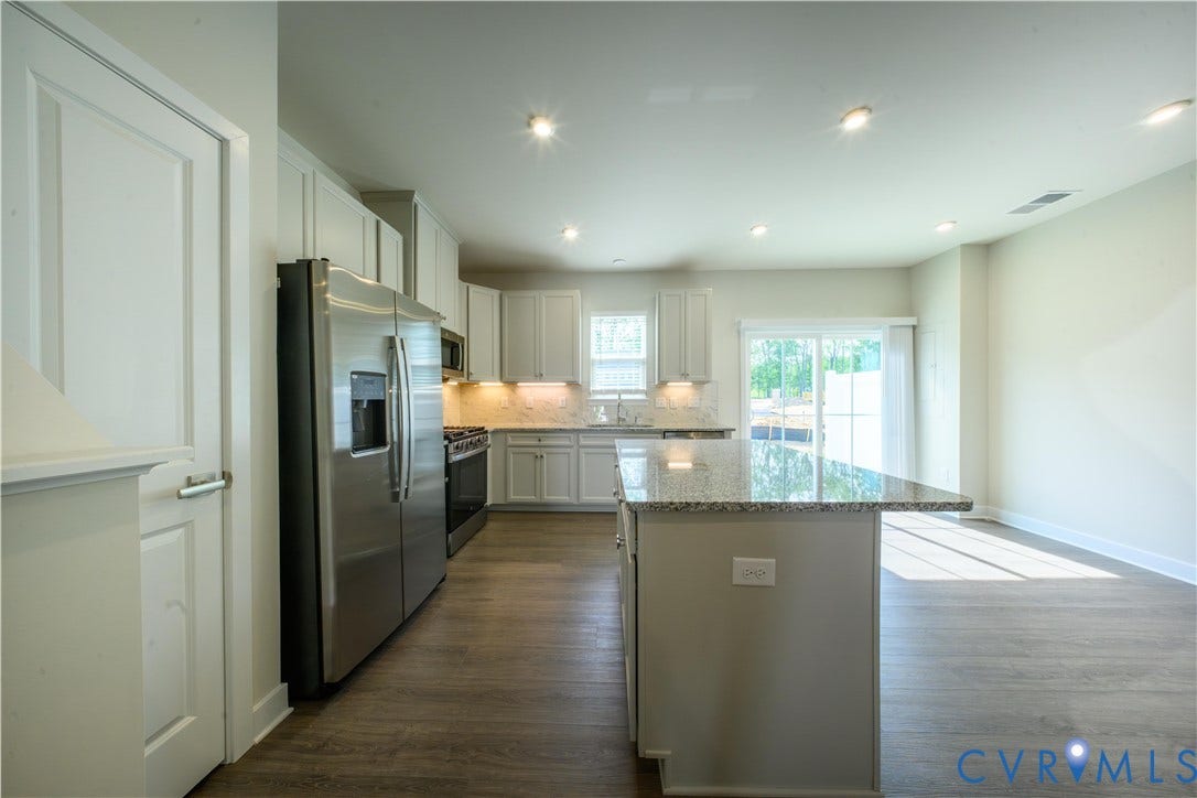 Kitchen featuring white cabinetry, stainless steel appliances, a center island with a speckled countertop, and wood-finish flooring