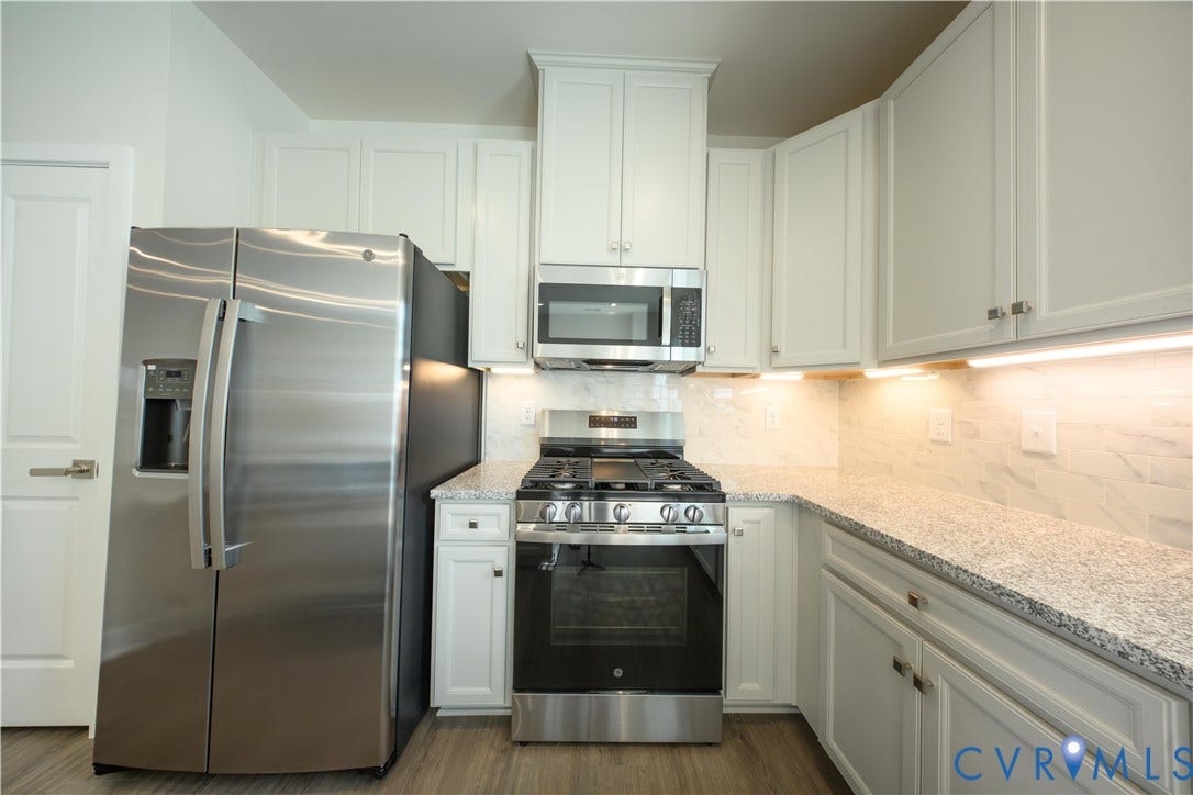 Stainless steel appliances, light-toned cabinetry, solid surface countertops, tile backsplash, and wood-finish flooring