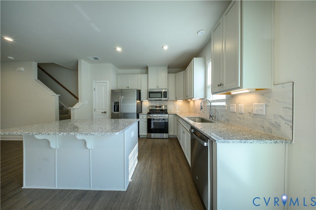 Kitchen featuring a large island, stainless steel appliances, light-toned cabinetry, granite countertops, and wood-finish flooring