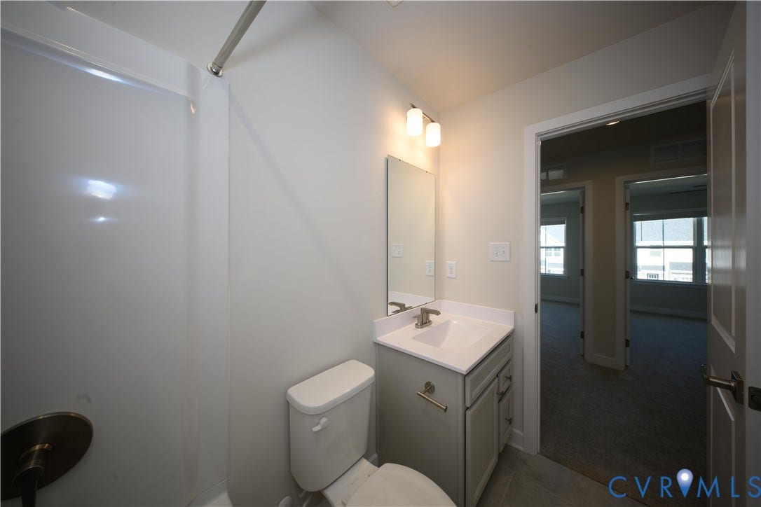 Shower-tub combination with brushed bronze shower head, single vanity with integrated sink, and wall-mounted mirror with overhead lighting