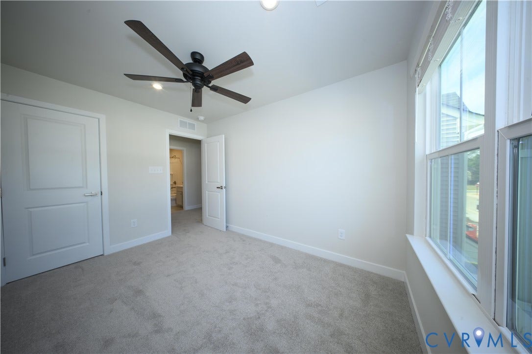 Plush carpet flooring, ceiling fan with dark wood-finish blades, recessed lighting, and large windows with white trim