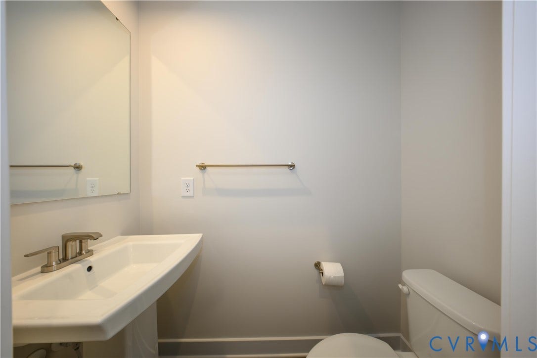 Pedestal sink with a brushed nickel faucet, wall-mounted mirror, and a toilet