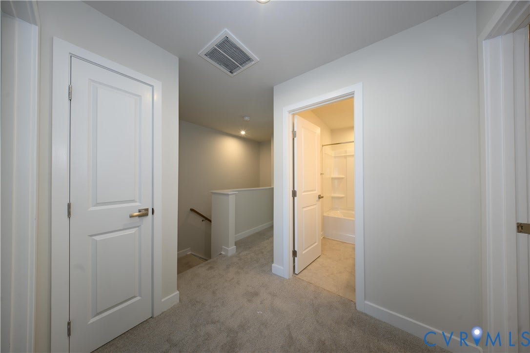 Carpeted hallway with white interior doors, recessed lighting, and a partial view of a bathroom with a white shower/tub combo