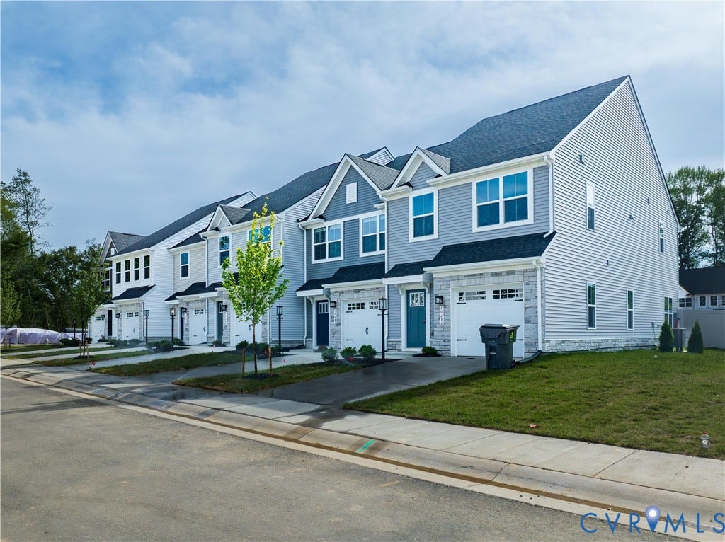 Row of townhomes featuring varied siding colors, white trim, attached garages, and individual front entrances