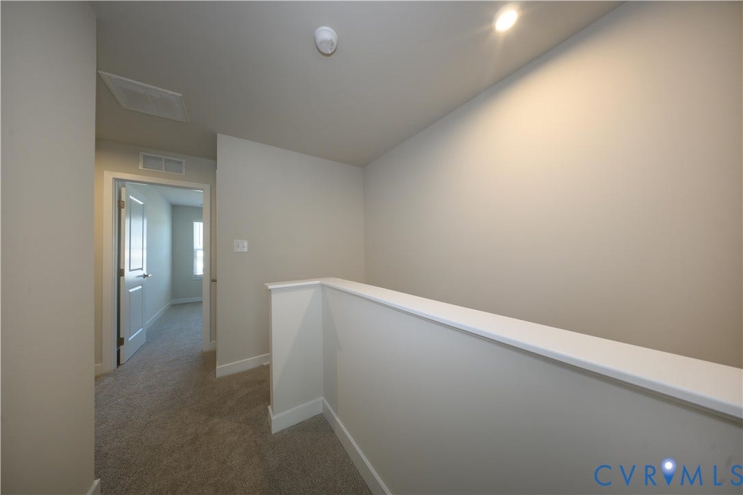 Carpeted hallway with light-toned walls, white trim, recessed lighting, and a white interior door