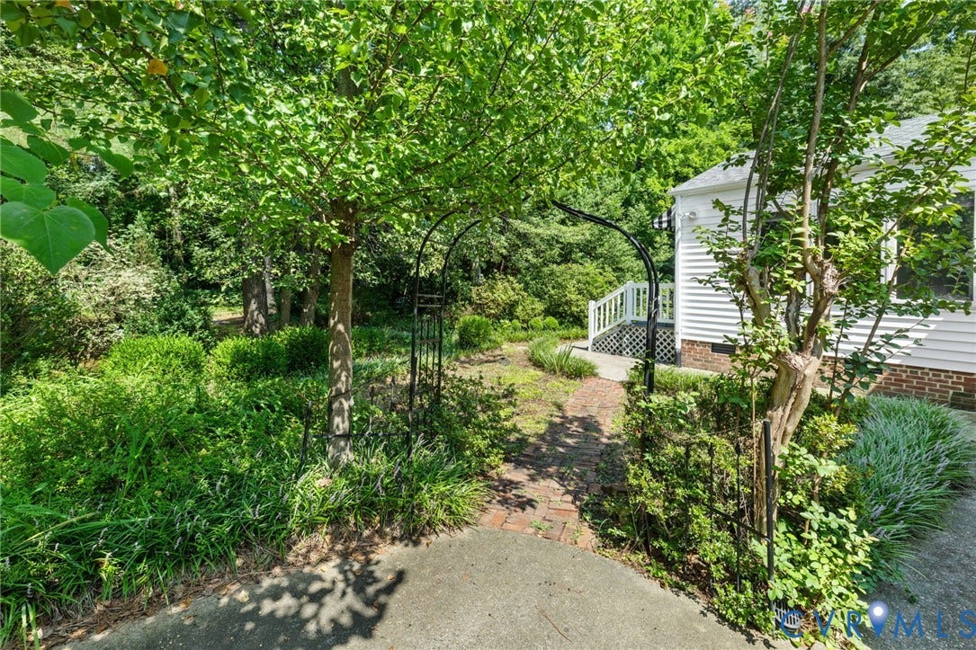 8208 Michael Road, Henrico, VA 23229 Lush landscaping with mature trees, a brick pathway, and a decorative metal archway