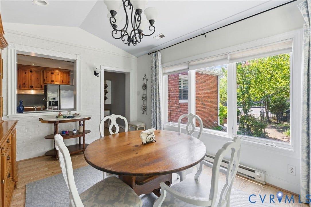 8208 Michael Road, Henrico, VA 23229 Vaulted ceiling with an ornate chandelier, large windows with roller shades, wood-finish flooring, and a pass-through opening to the kitchen featuring wood cabinetry and stainless steel appliances