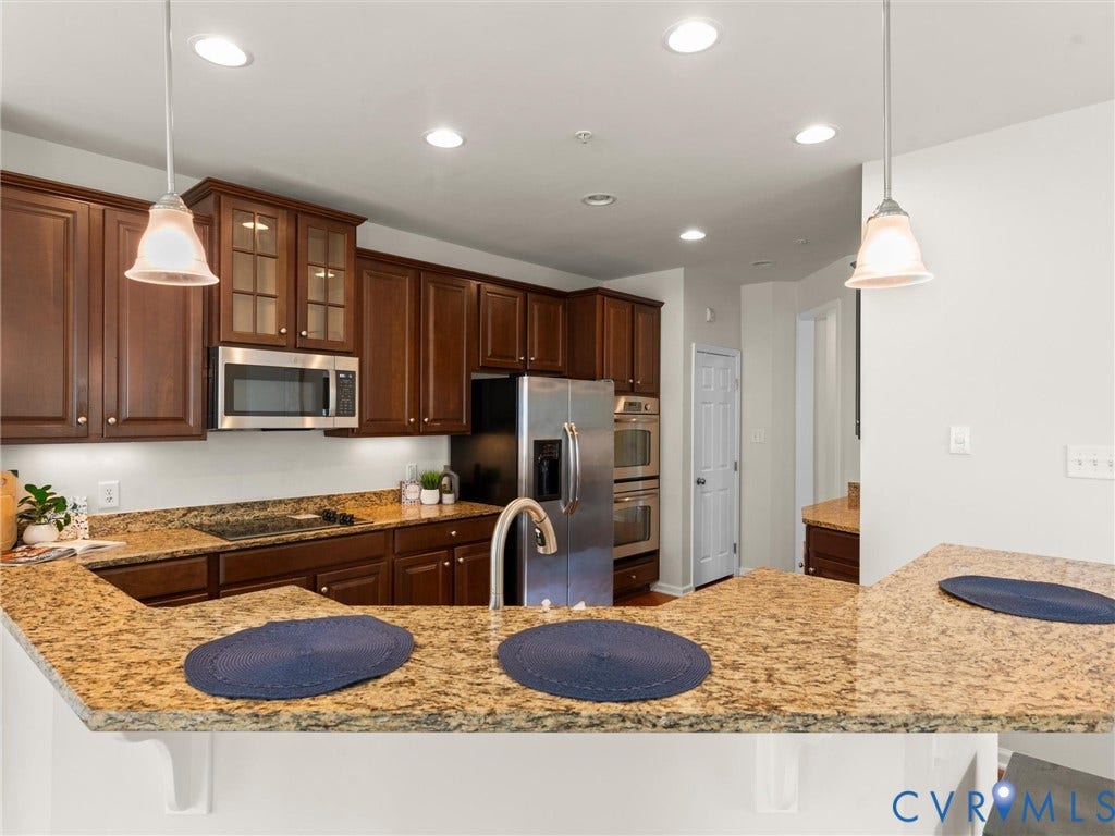 1901 Liesfeld Parkway, West Broad Village, Glen Allen, VA 23060 Kitchen featuring a large breakfast bar, brown wood cabinetry, light-toned countertops, stainless steel appliances, and recessed lighting