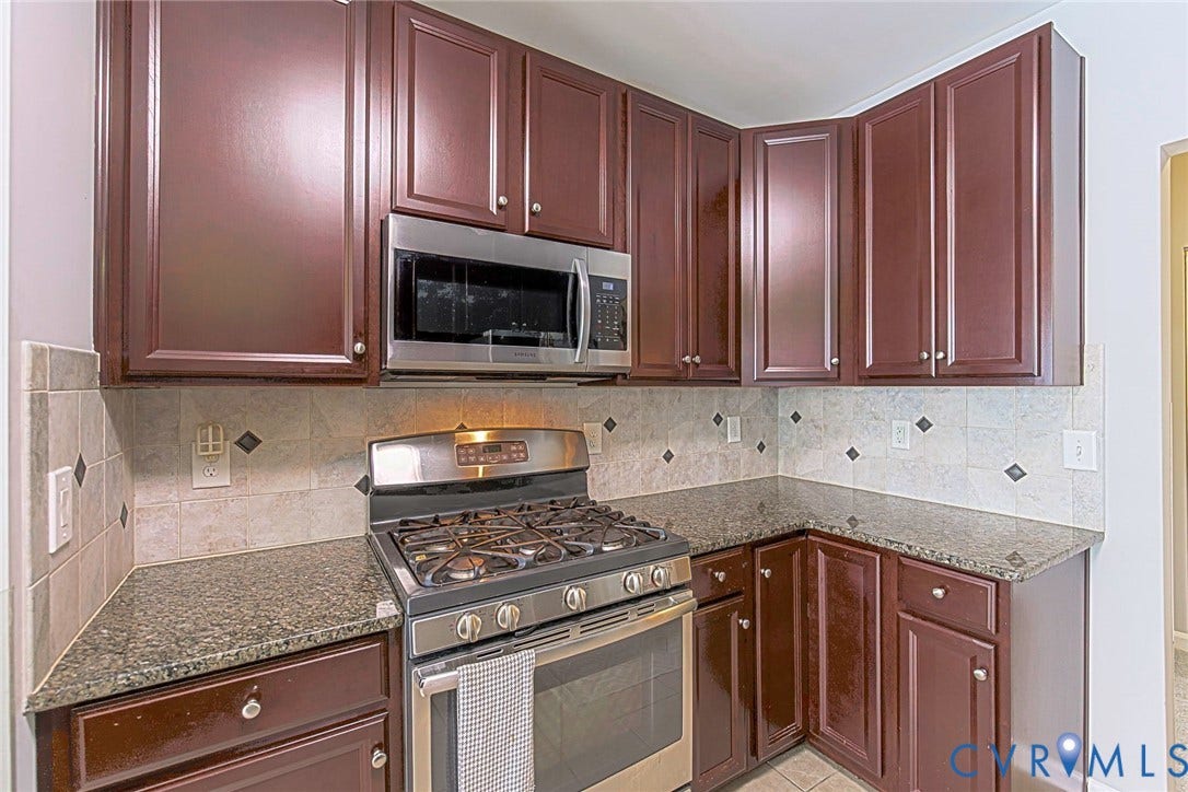 Rich wood-finish cabinetry with silver hardware, stone countertops, stainless steel gas range, stainless steel microwave, and tiled backsplash