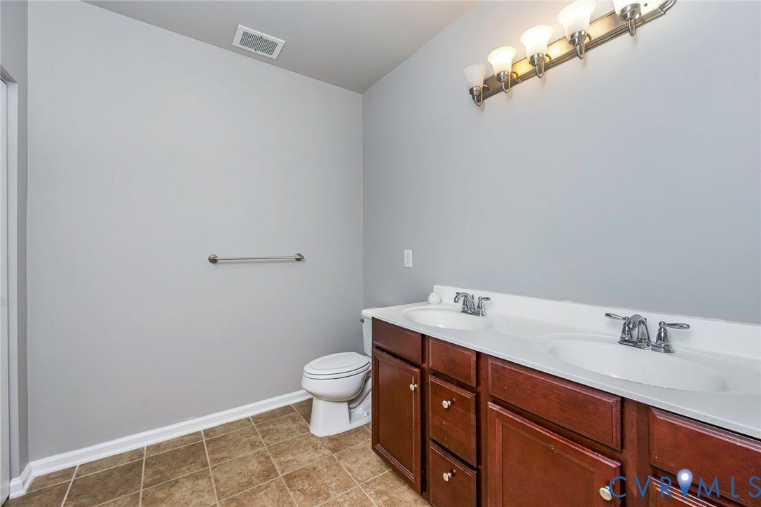 Dual vanity with wood-finish cabinetry, white countertop, and polished chrome fixtures