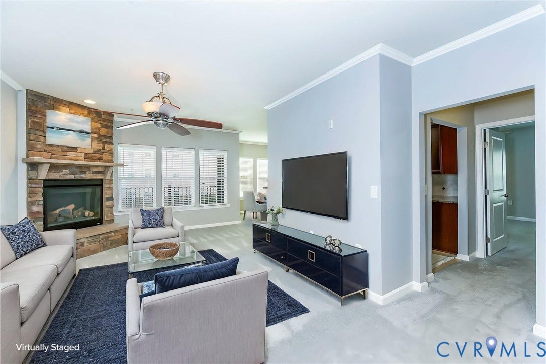 Living area featuring a stone-clad fireplace with a mantel, crown molding, a ceiling fan- virtually staged