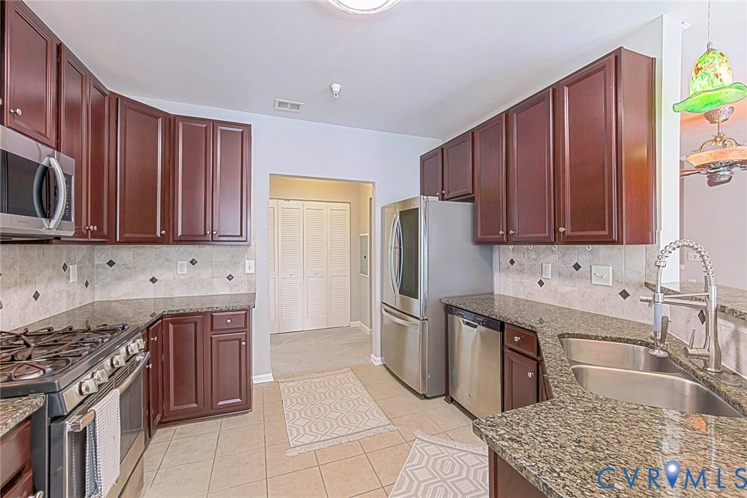 Tile flooring, dark wood-finish cabinetry, stainless steel appliances, granite countertops, and a tile backsplash