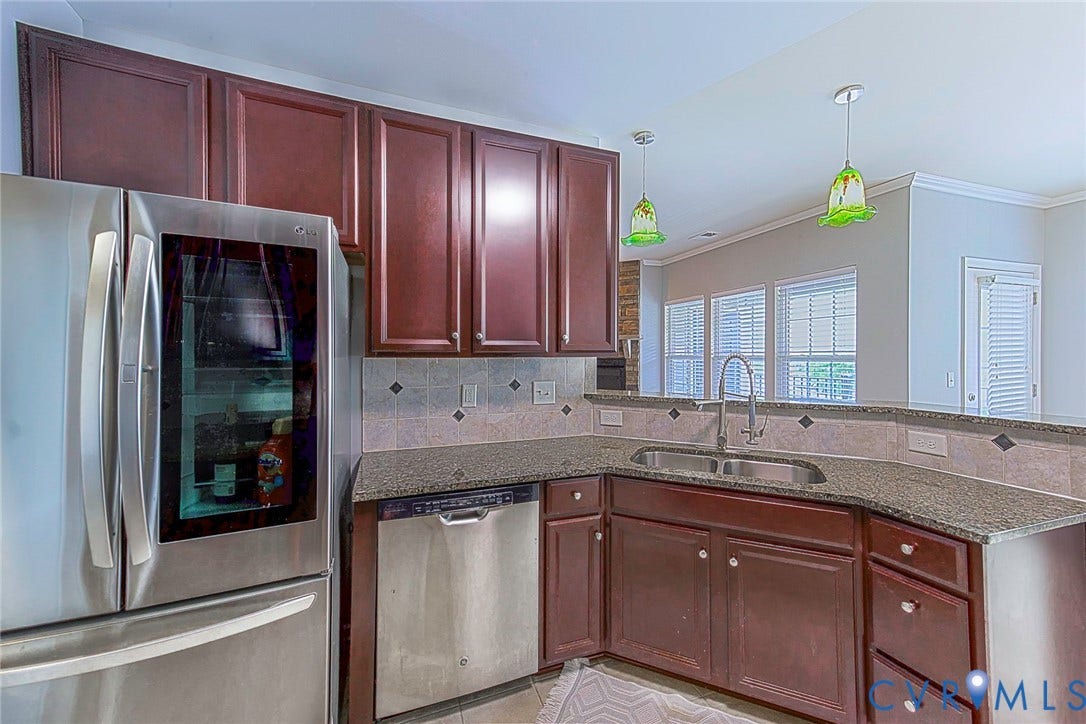Kitchen featuring stainless steel appliances, dark wood-finish cabinetry, stone countertops, and tile backsplash