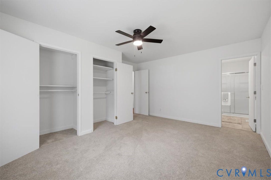 2338 Georges Road, Powhatan, VA 23139 Carpeted room with a ceiling fan, two closet openings with shelving and hanging rods, and a doorway leading to a bathroom with a shower enclosure