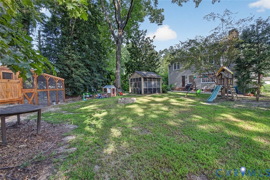 Expansive backyard oasis featuring mature shade trees, manicured lawn, and multiple recreational structures including a wooden-frame outbuilding, play equipment, and detached garage