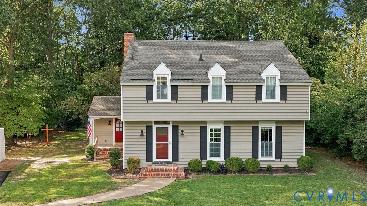 Classic Colonial-style home featuring a symmetrical facade with three dormers, brick front walkway, and manicured lawn anchored by mature landscaping