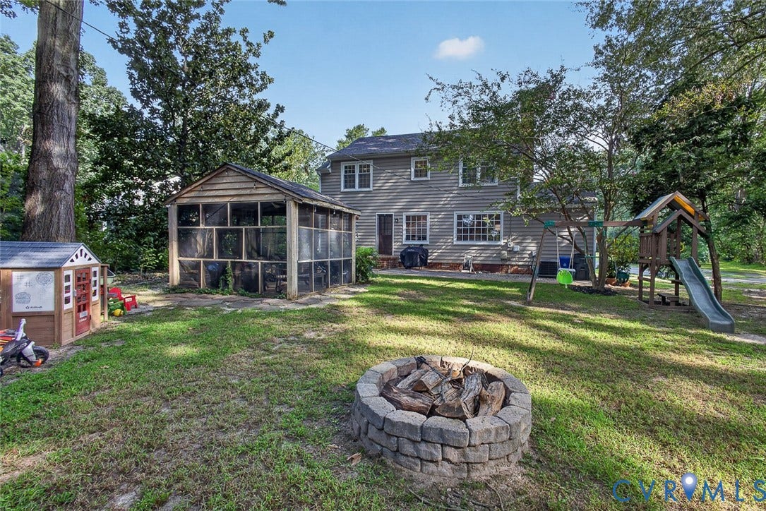 Expansive backyard featuring a screened-in structure, mature trees, and a stone-lined fire pit
