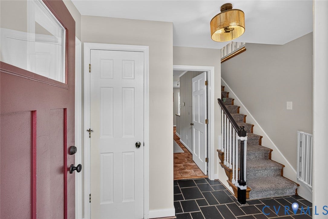 Foyer featuring slate flooring, a wood-paneled door with transom window, and a carpeted staircase with wood banister