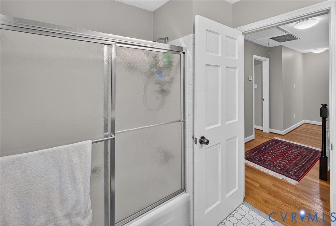 Frosted glass shower enclosure with a white tub, white panel door, and hardwood flooring