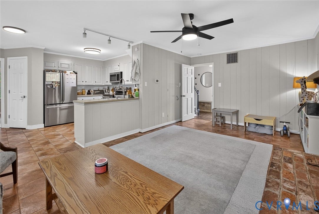 Open-concept living area with light gray vertical paneling and a matte black ceiling fan