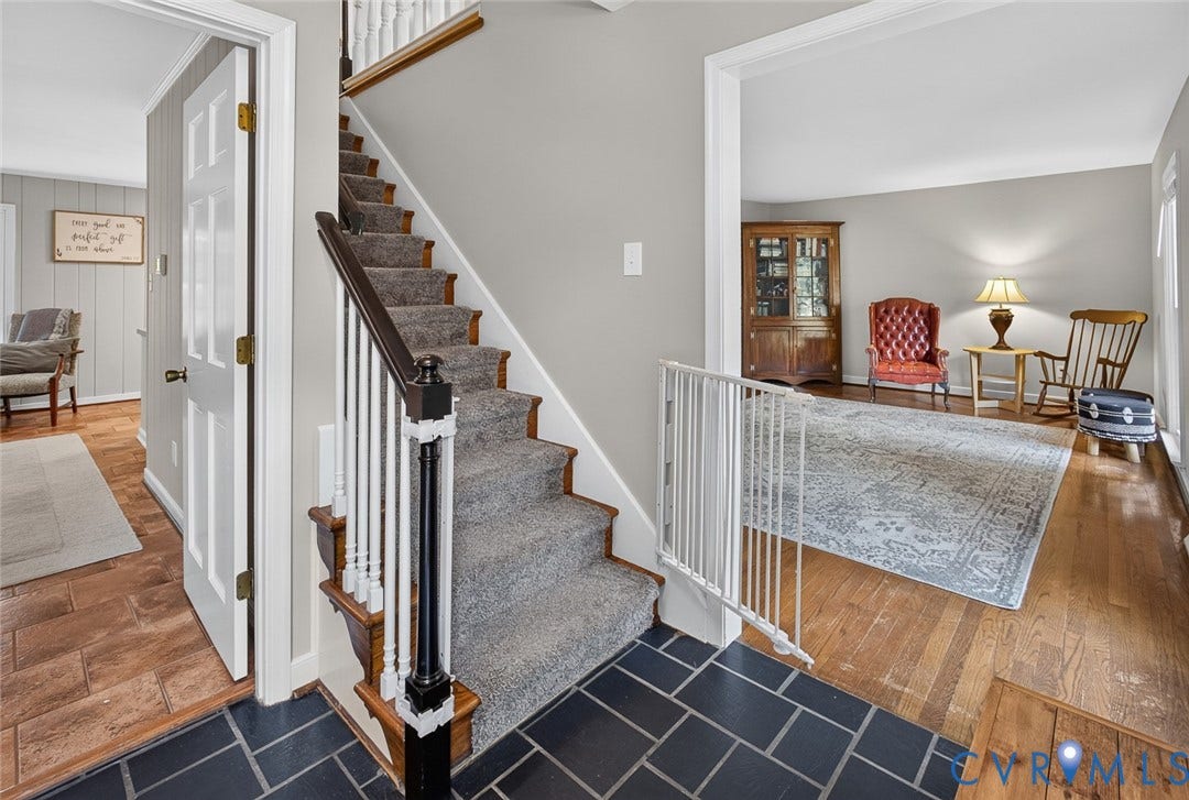 Foyer with dark slate tile flooring, a carpeted staircase with wood handrails, and a paneled white door
