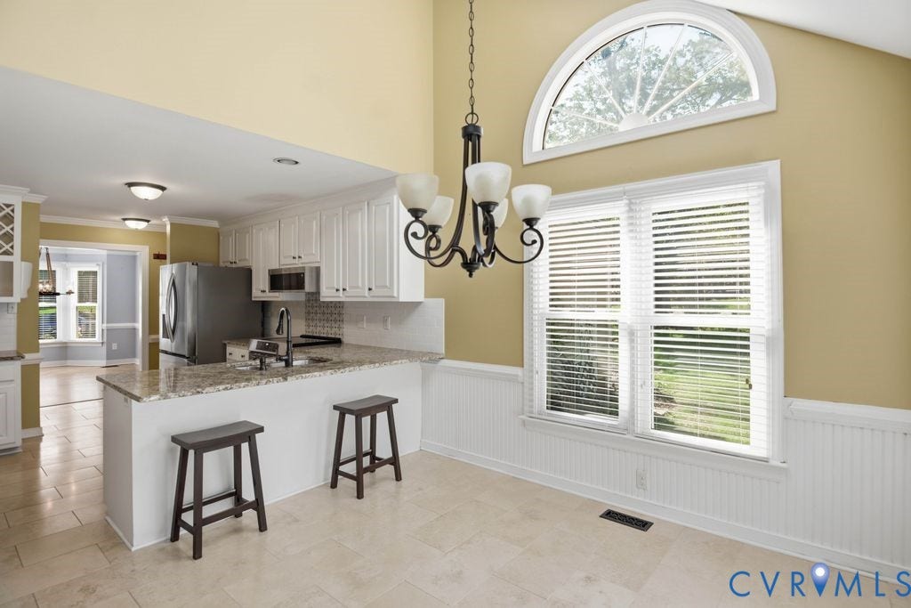 8806 Thornton Heath Drive, Chesterfield, VA 23832 Vaulted ceiling with an arched transom window, a breakfast bar featuring a speckled countertop, tile flooring, and white wainscoting