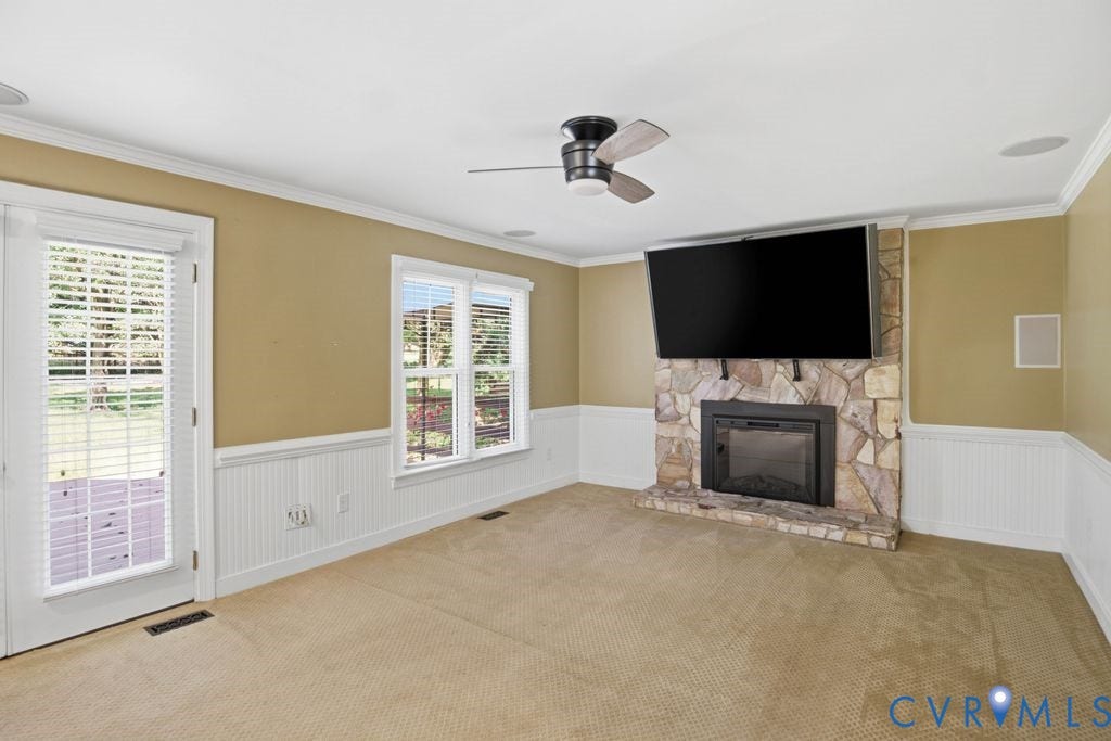 8806 Thornton Heath Drive, Chesterfield, VA 23832 Stone fireplace with a black firebox, ceiling fan with wood-finish blades, white wainscoting, and crown molding