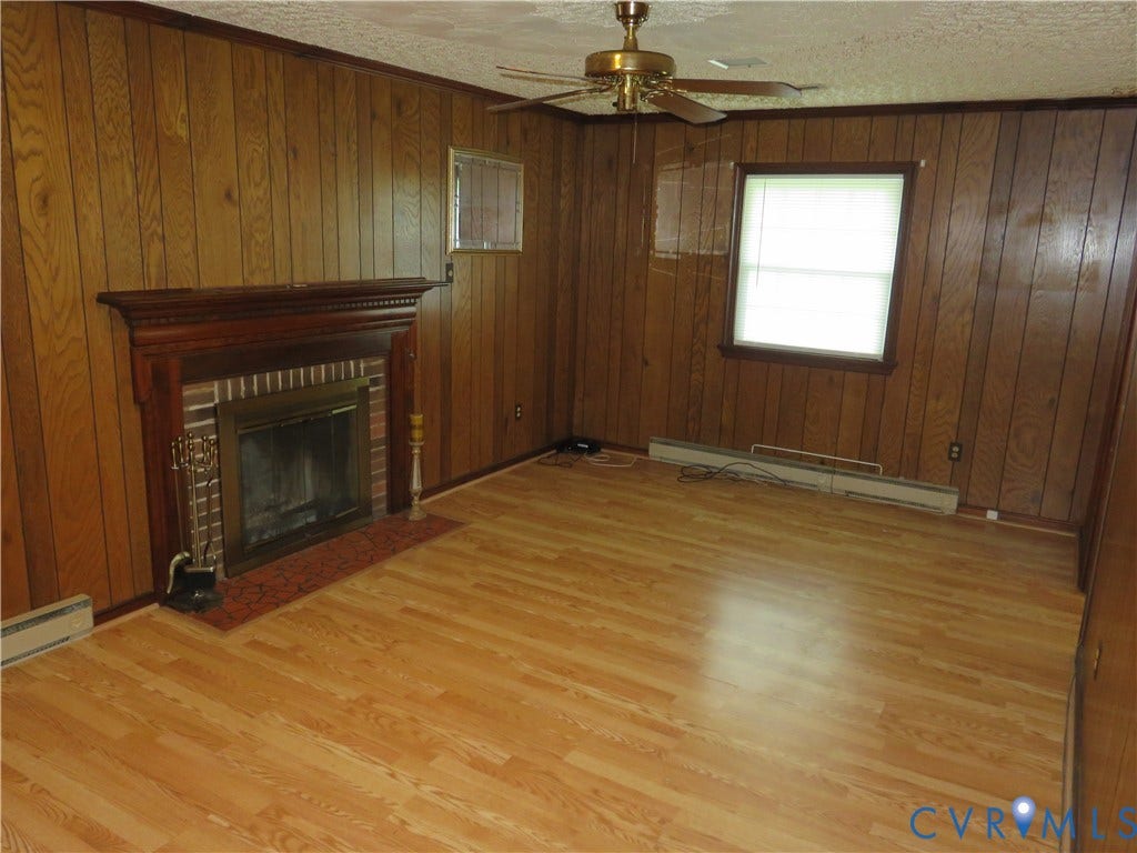 3107 Neale Street, Eastern Henrico, Richmond, VA 23223 Wood-finish flooring, wood paneling, brick fireplace with a wood mantle, ceiling fan, and a window with blinds