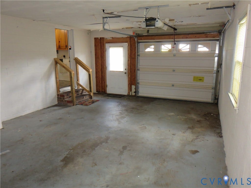 3107 Neale Street, Eastern Henrico, Richmond, VA 23223 Attached garage with a roll-up door, interior access door, staircase with wood railings, and an upper-level cabinet installation