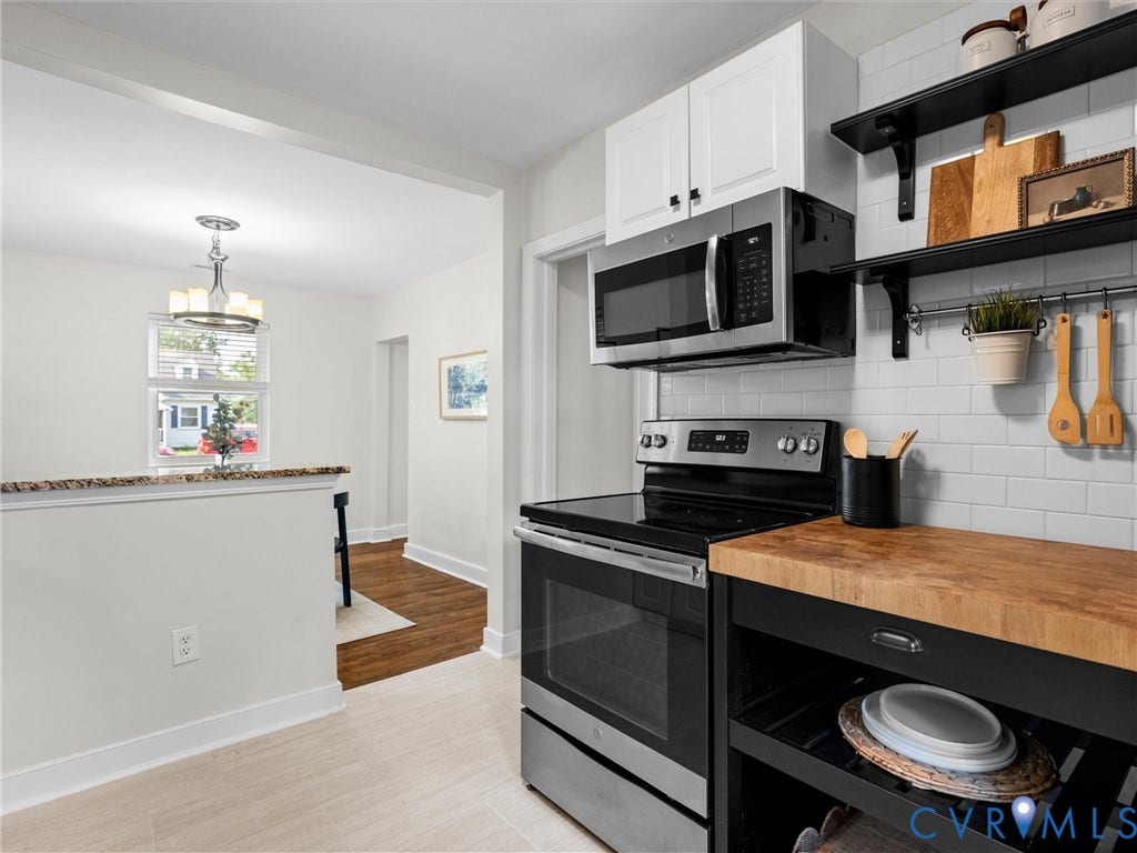 709 Ratcliffe Avenue, Richmond, VA 23222 Stainless steel microwave and range, white subway tile backsplash, white upper cabinetry, butcher block countertop on a black island, and light-toned tile flooring