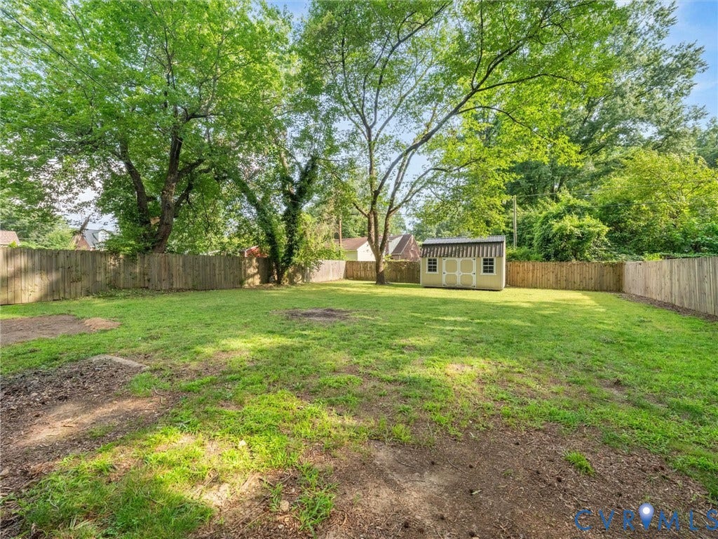 709 Ratcliffe Avenue, Richmond, VA 23222 Expansive backyard featuring a privacy fence, mature trees, and a detached storage shed with awning details