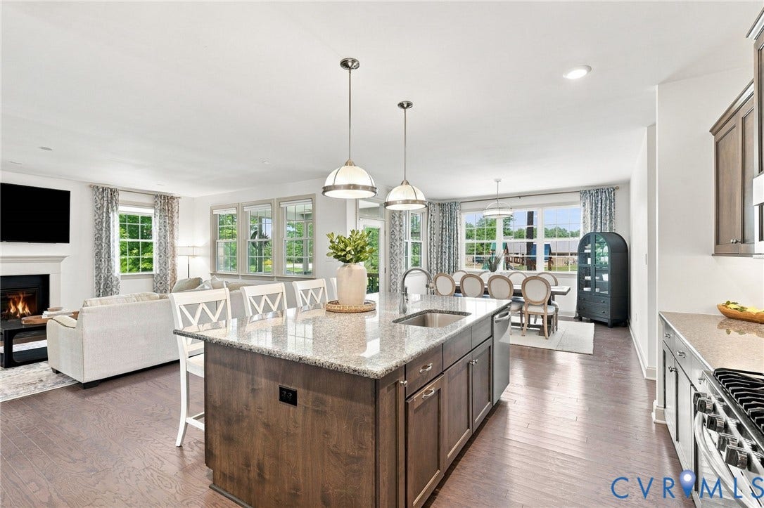 6907 Carden Park Drive, Carden Park, Moseley, VA 23120 Open-concept living space featuring hardwood flooring, a kitchen island with seating, a built-in fireplace, and expansive window placements