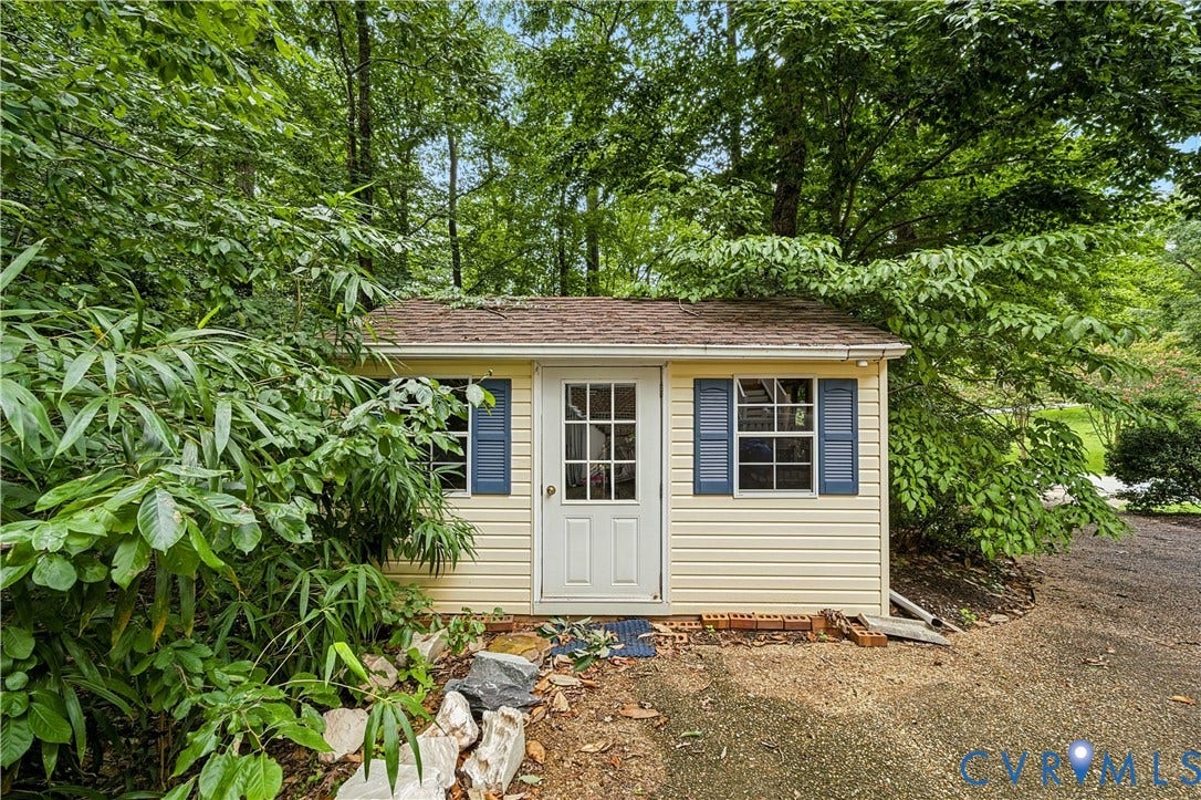 411 Hickory Drive, Manakin Sabot, VA 23103 Storage shed featuring vertical siding, a paneled entry door, two windows with louvered shutters, and a shingled roof
