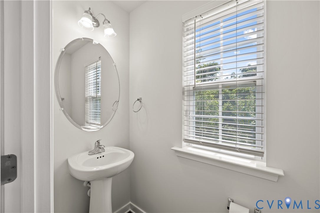 3372 Dewsberry Lane, Henrico, VA 23231 Pedestal sink, oval mirror, wall-mounted light fixture, and window with blinds