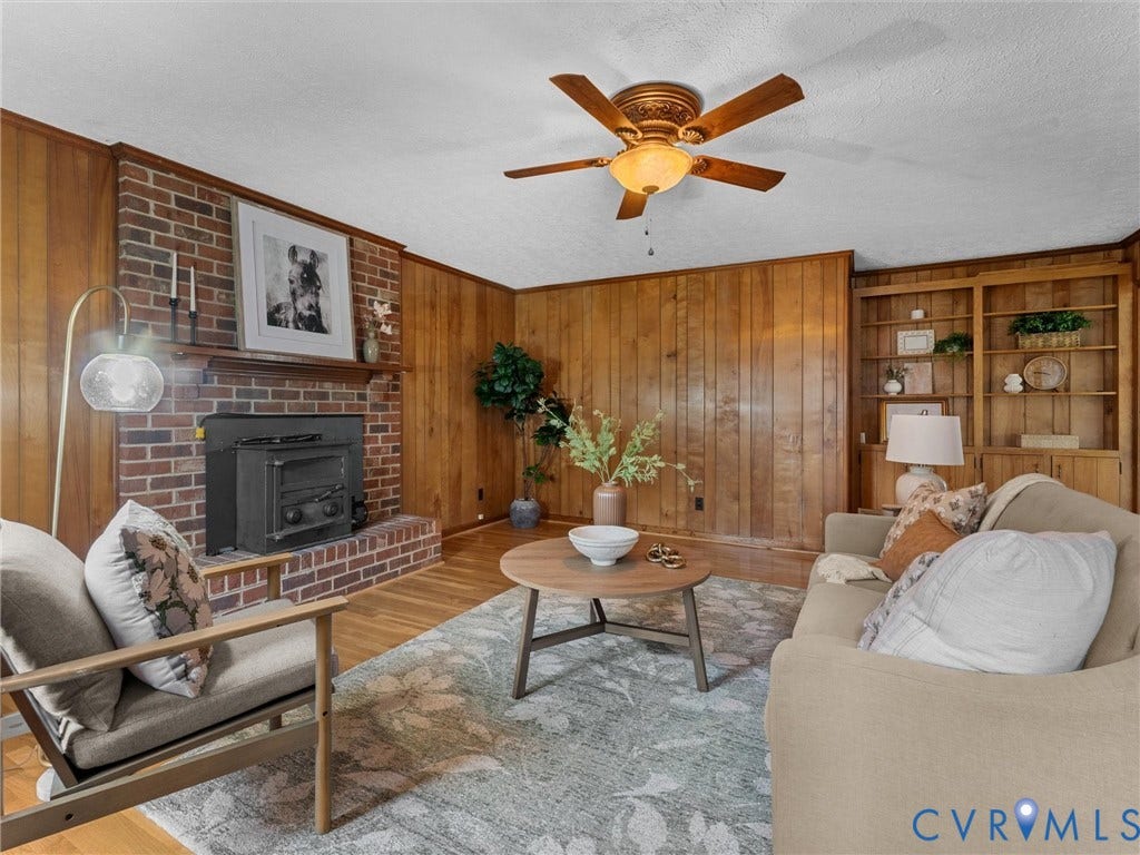 3610 Castlebury Drive, Chester, VA 23831 Brick fireplace with an insert, wood paneling, wood-finish flooring, built-in shelving, and a ceiling fan