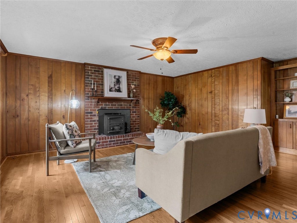 3610 Castlebury Drive, Chester, VA 23831 Wood paneling accent walls, brick fireplace with mantel, wood-finish flooring, built-in shelving, and a ceiling fan with light fixture