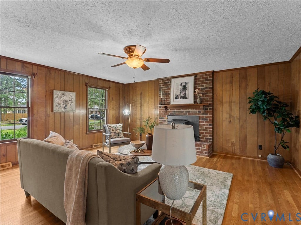 3610 Castlebury Drive, Chester, VA 23831 Brick fireplace with a wood mantle, wood-paneled walls, hardwood flooring, and a ceiling fan