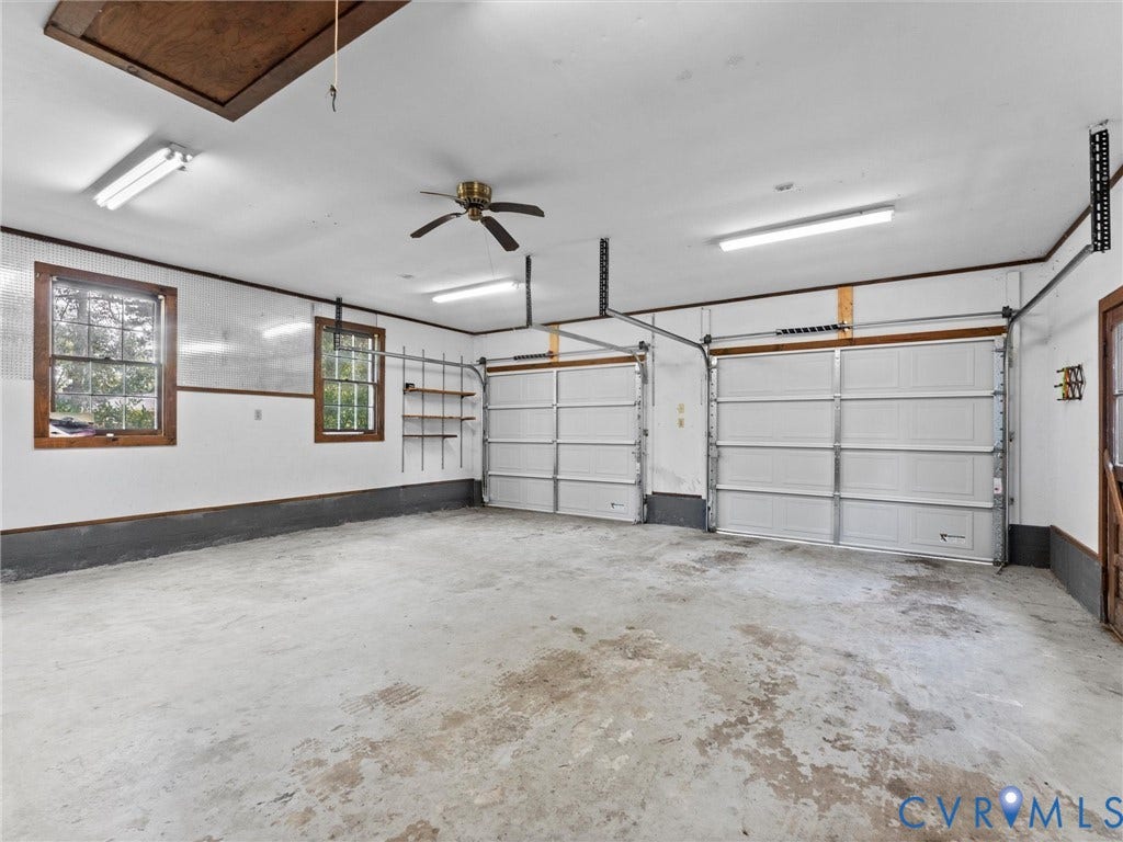 3610 Castlebury Drive, Chester, VA 23831 Two-car garage with concrete flooring, dual overhead garage doors, two windows with wood trim, built-in shelving, and a ceiling fan