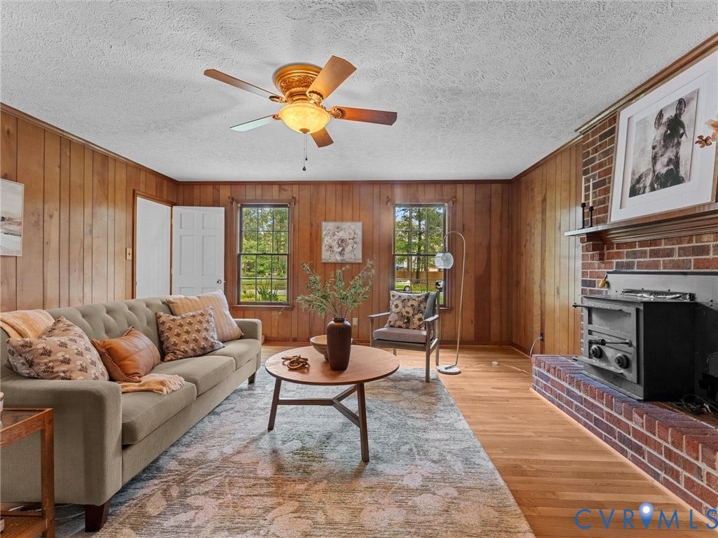 3610 Castlebury Drive, Chester, VA 23831 Brick fireplace with wood-burning stove insert, wood-paneled walls, wood-finish flooring, and ceiling fan with integrated lighting