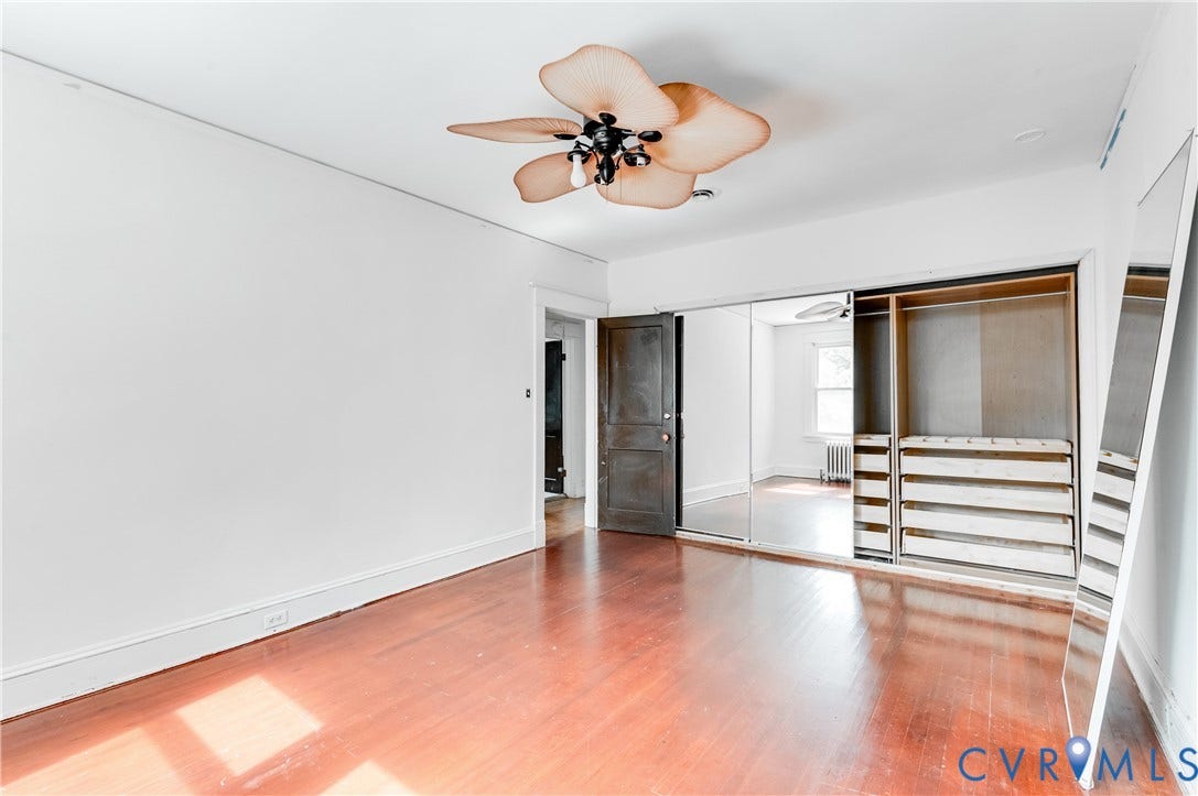 Wood-finish flooring, ceiling fan with integrated lighting, built-in closet system with drawers and shelving, mirrored closet doors, and painted white walls