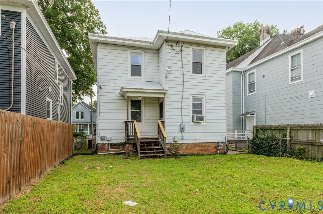 Rear exterior with light-colored siding, wood stairs, and a grassy backyard