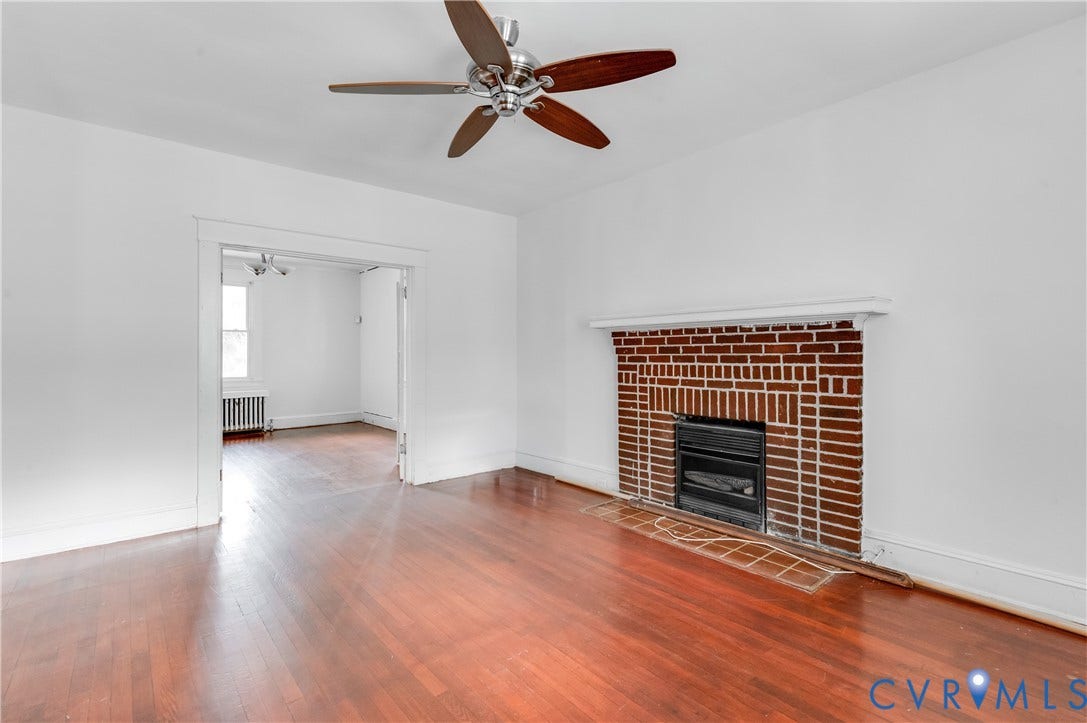 Hardwood flooring throughout, brick fireplace with a tile hearth, and a ceiling fan with integrated lighting
