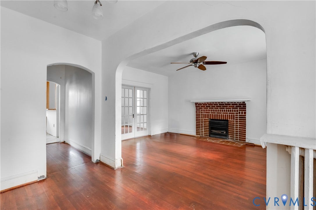 Hardwood flooring, arched doorways, brick-faced fireplace with hearth and mantel, ceiling fan, and French doors