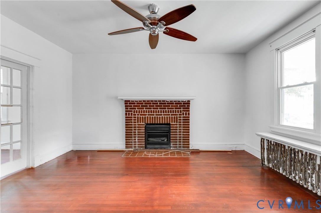 Hardwood flooring throughout, brick fireplace with mantel, ceiling fan, white trim, and a multi-pane window